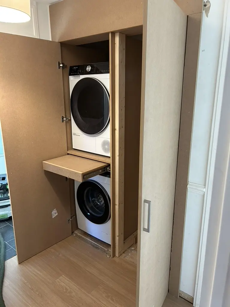 Built-in cupboard open, tumble dryer stacked above a washing machine with a pull-out shelf