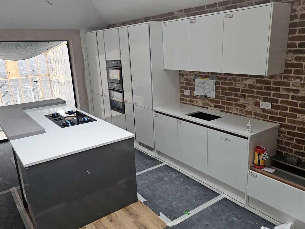 The same white gloss kitchen and island being fitted against the brick wall