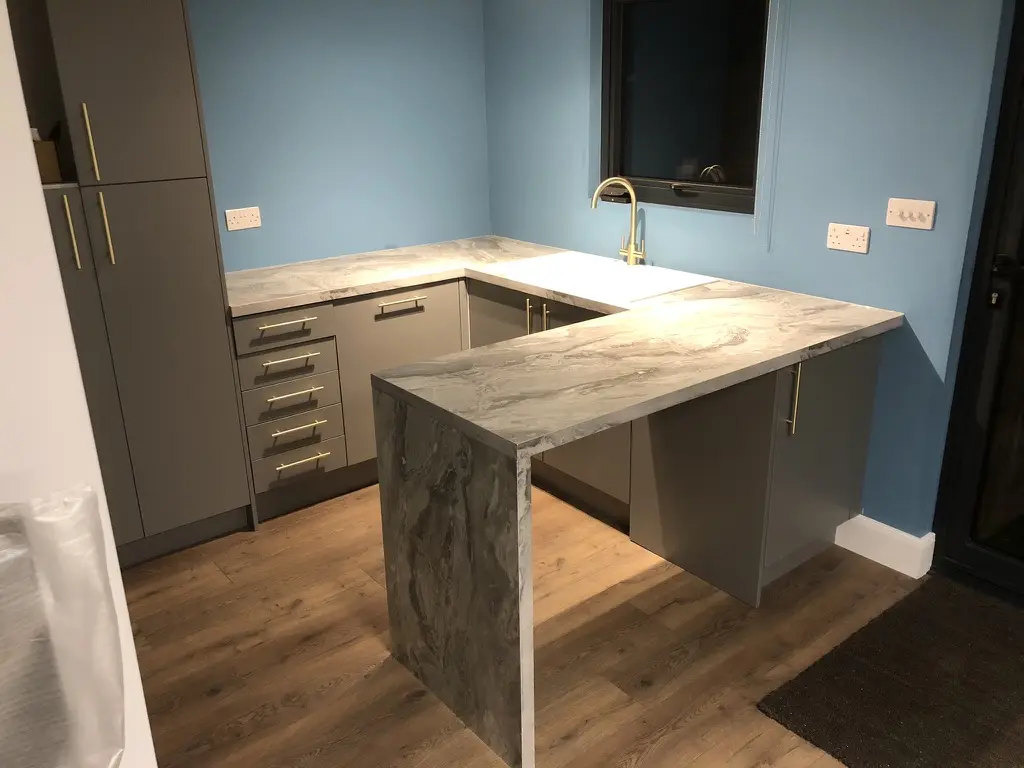 Grey kitchen with a marble-effect waterfall peninsula and brass bar handles