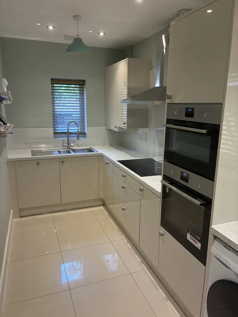 Cream gloss kitchen with double ovens, inset sink and stone-effect splashback