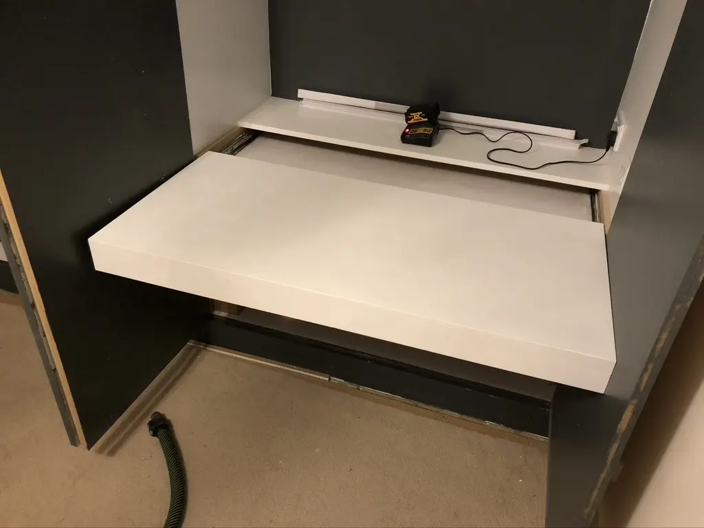 White pull-out desk on runners inside the cabinet, with a shelf and socket behind