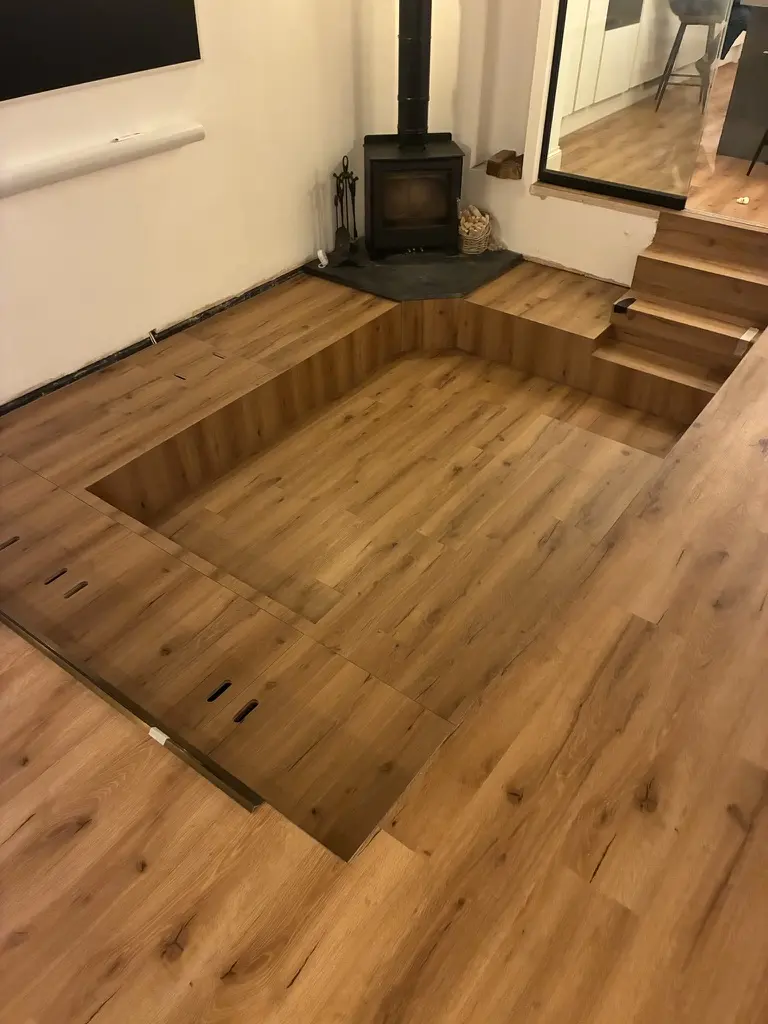 Sunken area with steps up to a raised corner hearth and wood burner