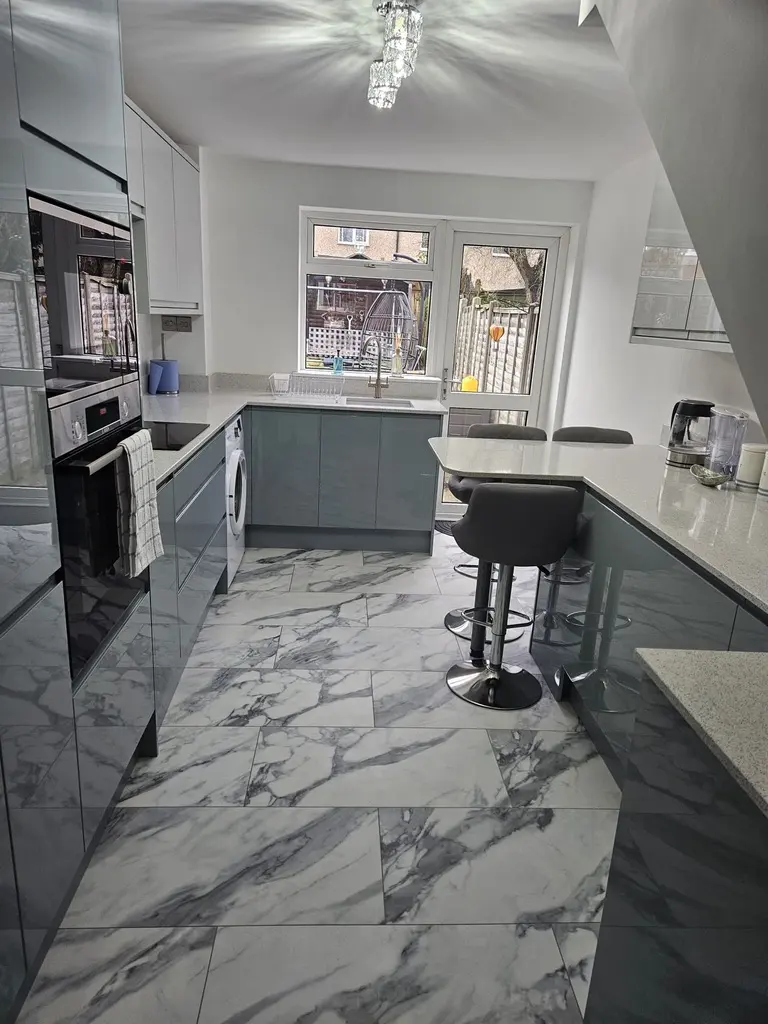Finished grey gloss handleless kitchen with breakfast bar and marble-effect floor tiles