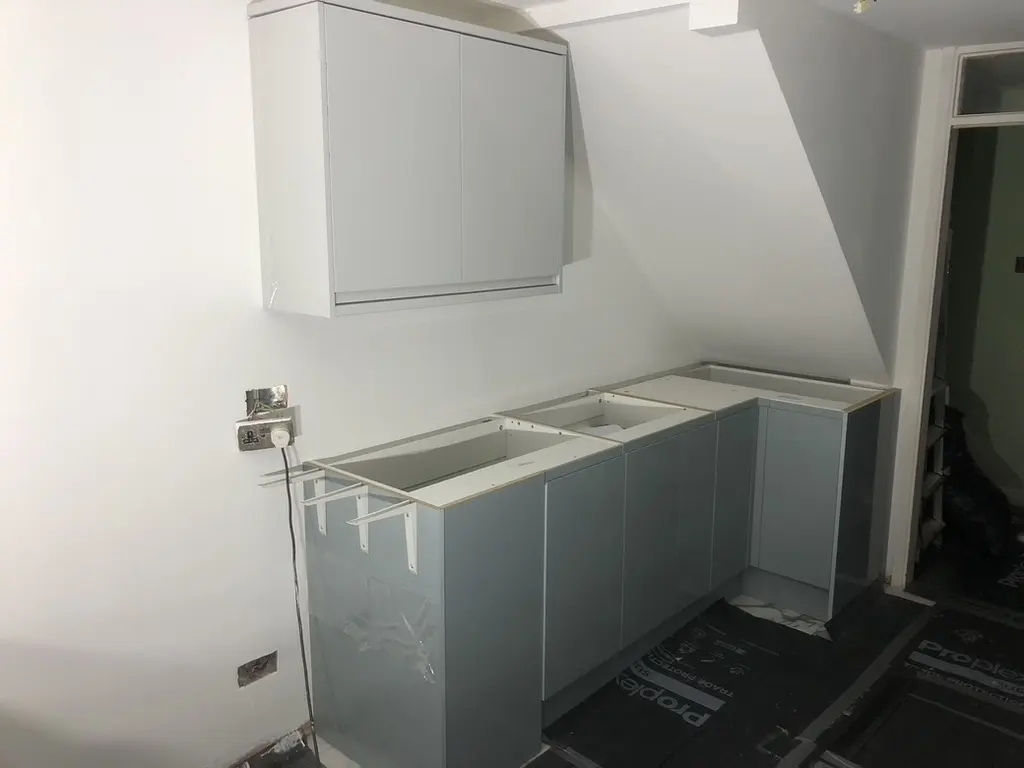 Grey gloss base units and wall cabinet fitted under the stairs, worktops not yet on